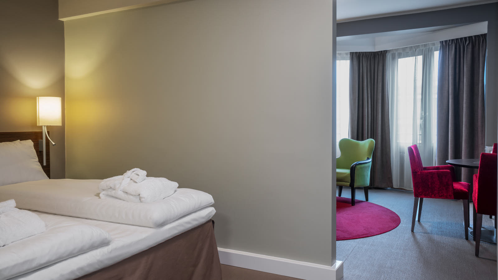 Dobbeltseng i rom med lyse grå vegger og åpen løsning ut mot oppholdsrom