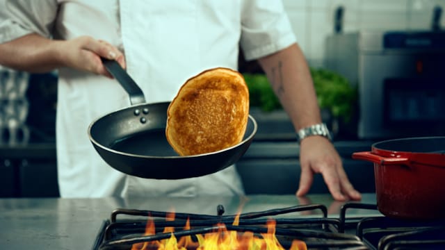 A chef flips a pancake over open flames