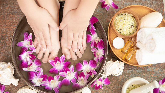 picture of a person with their feet in water with flowers and other wellness products next to them