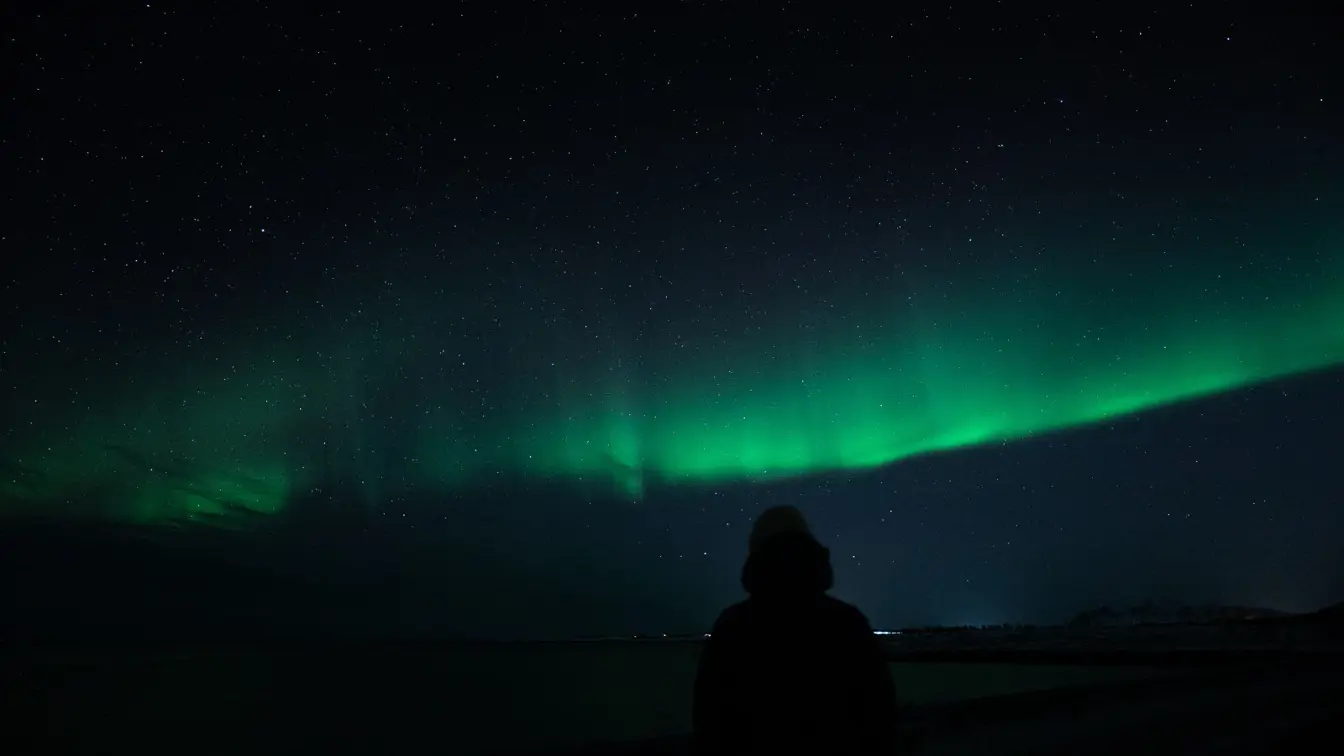 Tanzendes Nordlicht über einem dunklen Himmel mit Bergen am Horizont