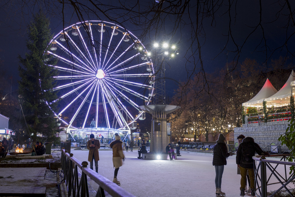 Nattscene med opplyst pariserhjul på vinterfestivalen med folk som går på snødekt sti og festlige høytidslys.