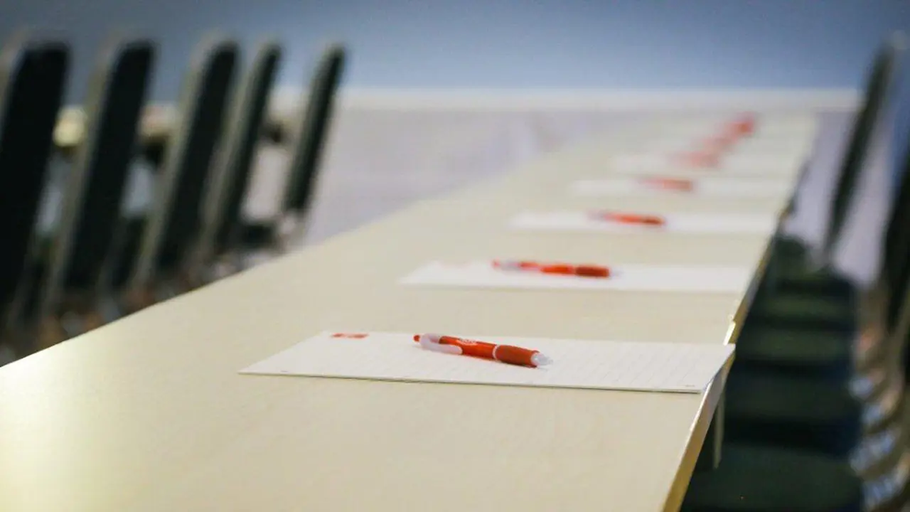 Close-up of a long desk covered with stationery and matching black chairs.