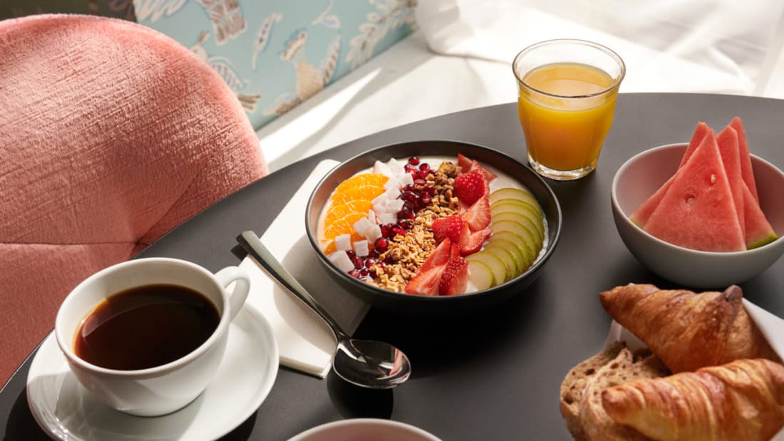 Detaljebillede af smoothiebowle, frugt, kaffe og bagværk på bordet