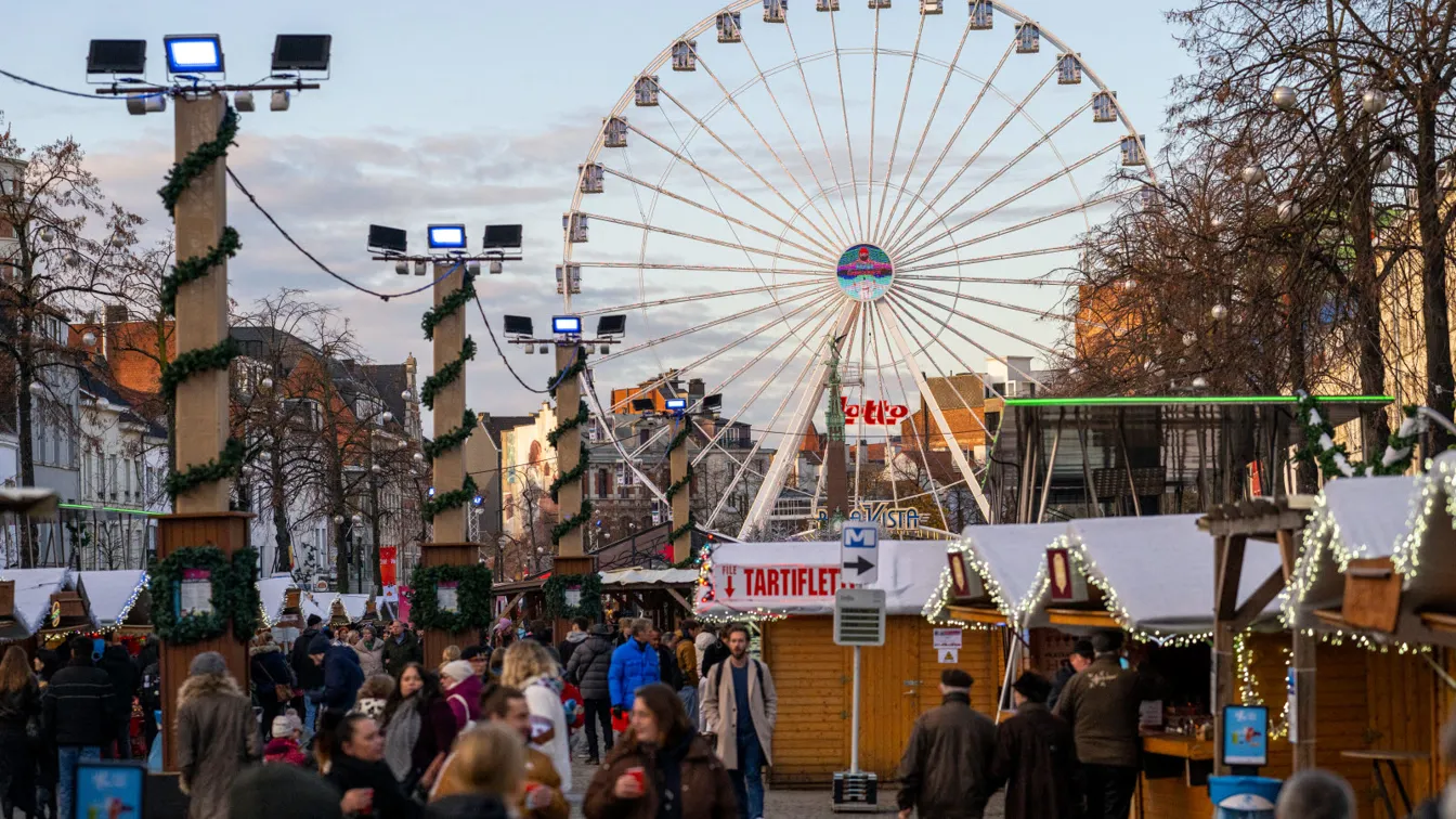 The Christmas market in Brussels, with sales booths to the right, a crowd to the left, and a Ferris wheel in the background.