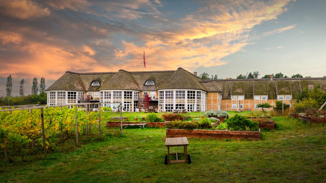 The facade of Thon Partner Hotel Sorø with a green garden in front of the hotel. Beautiful sunset in the background.