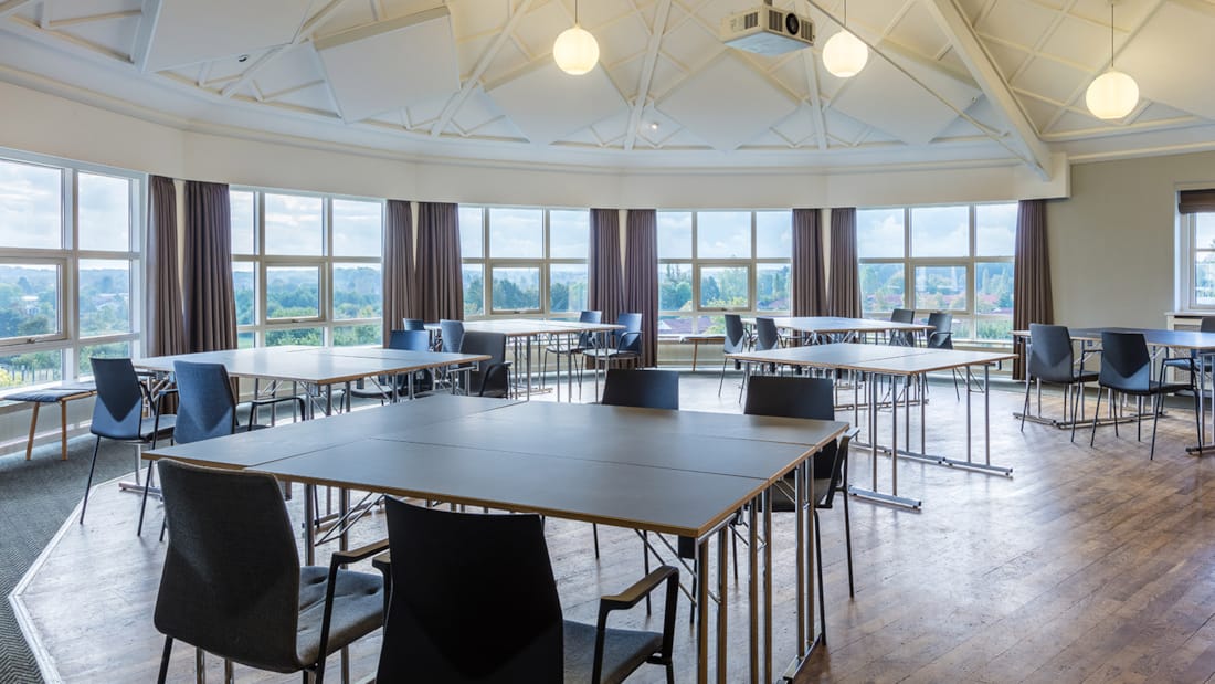 Meeting room with large windows. Tables and chairs arranged in groups. 