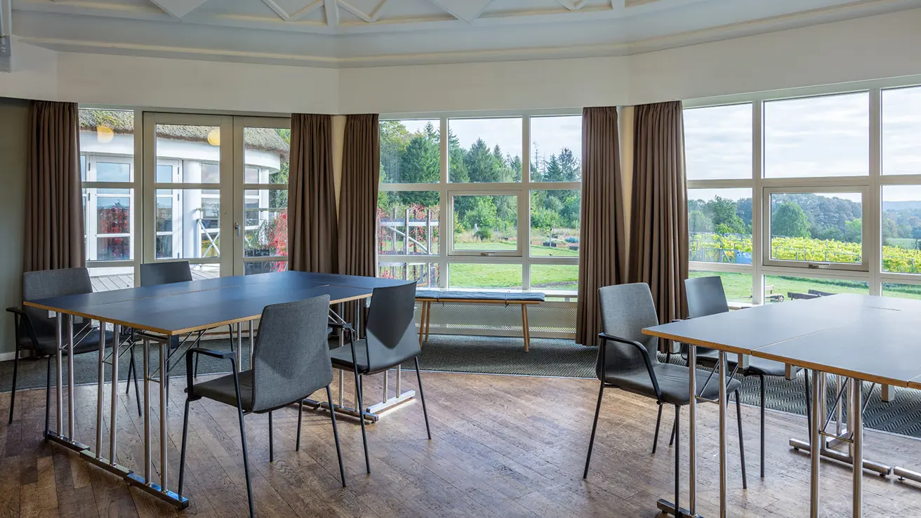 Bord og stoler i grupper i møterom med store vinduer og utsikt mot hage