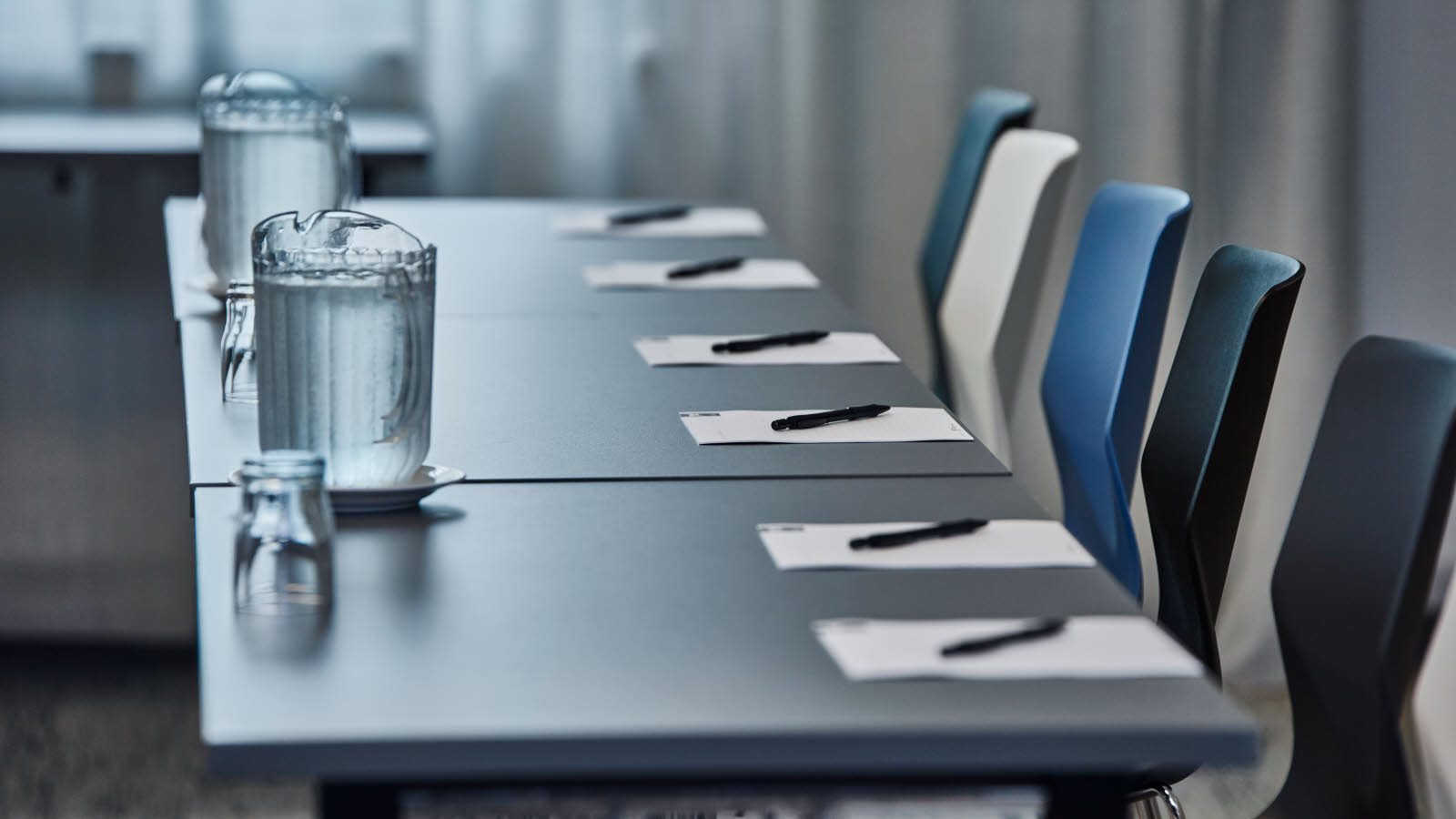 Close-up van bureaus en stoelen. De tafel is gedekt met schrijfwaren, een glas water en een waterkaraf.