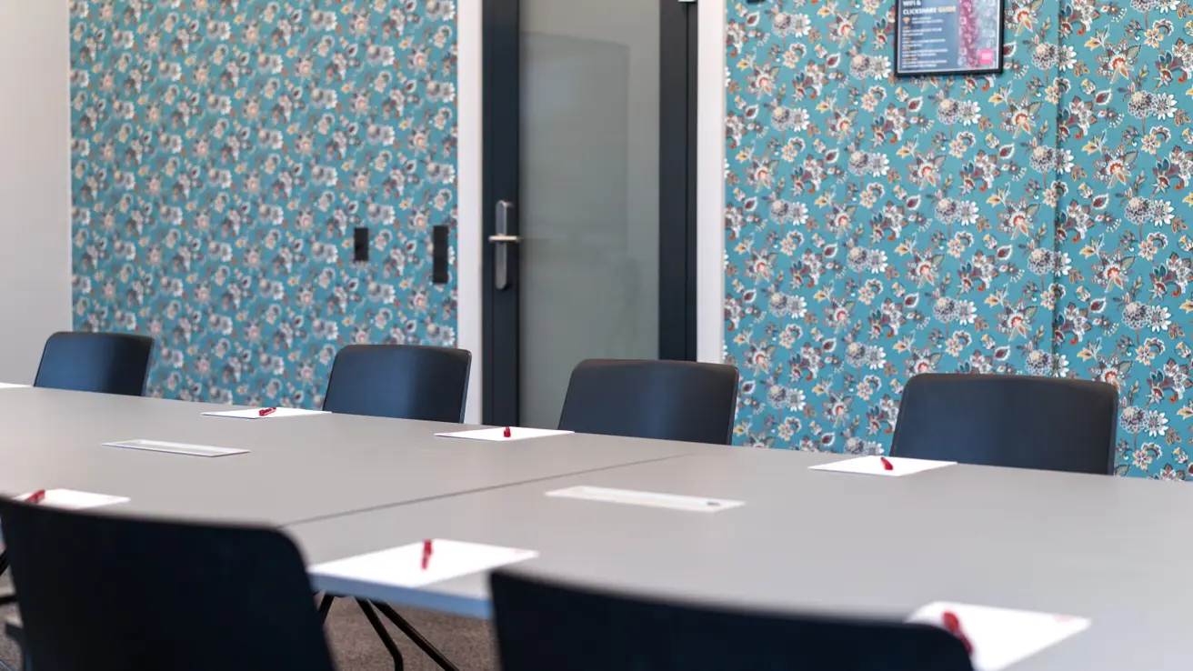 Salle de réunion avec mur de papier peint, bureau et chaises de bureau noires tout autour.