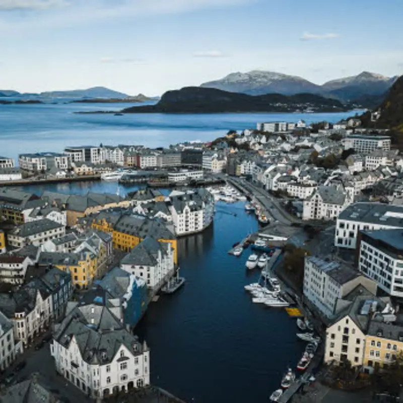 Oversiktsbilde over Ålesund by med havet og fjell i horisonten. Blå lettskyet himmel.