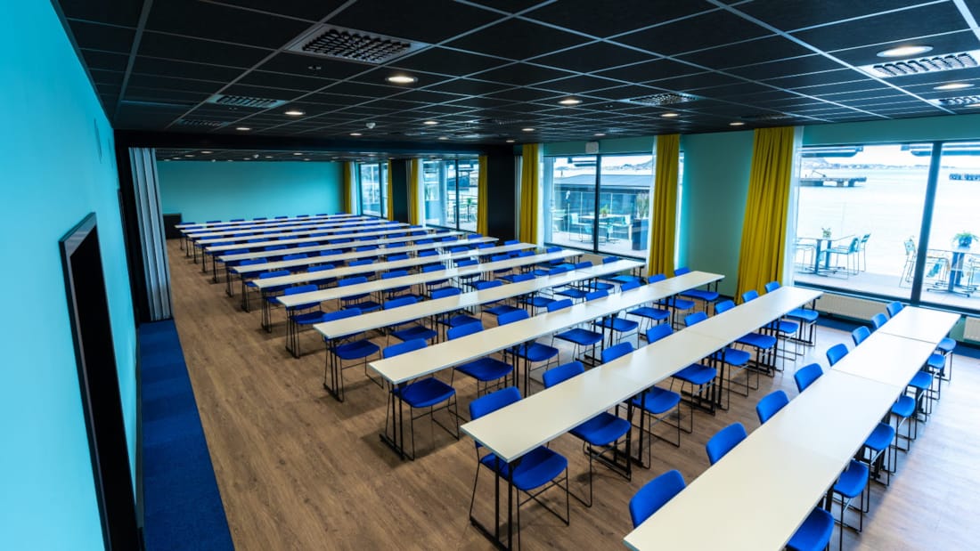 Mødelokale i klasseværelsesindretning med blå stole og store vinduer