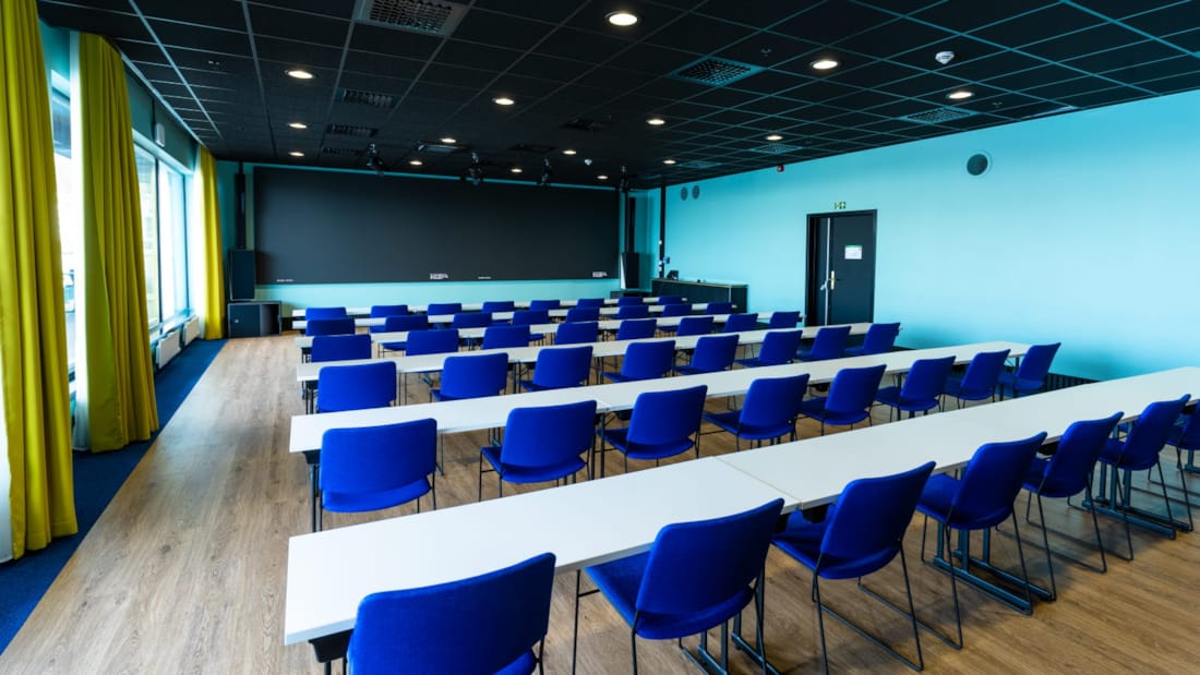 Salle de conférence en configuration salle de classe avec grandes fenêtres et tableau noir