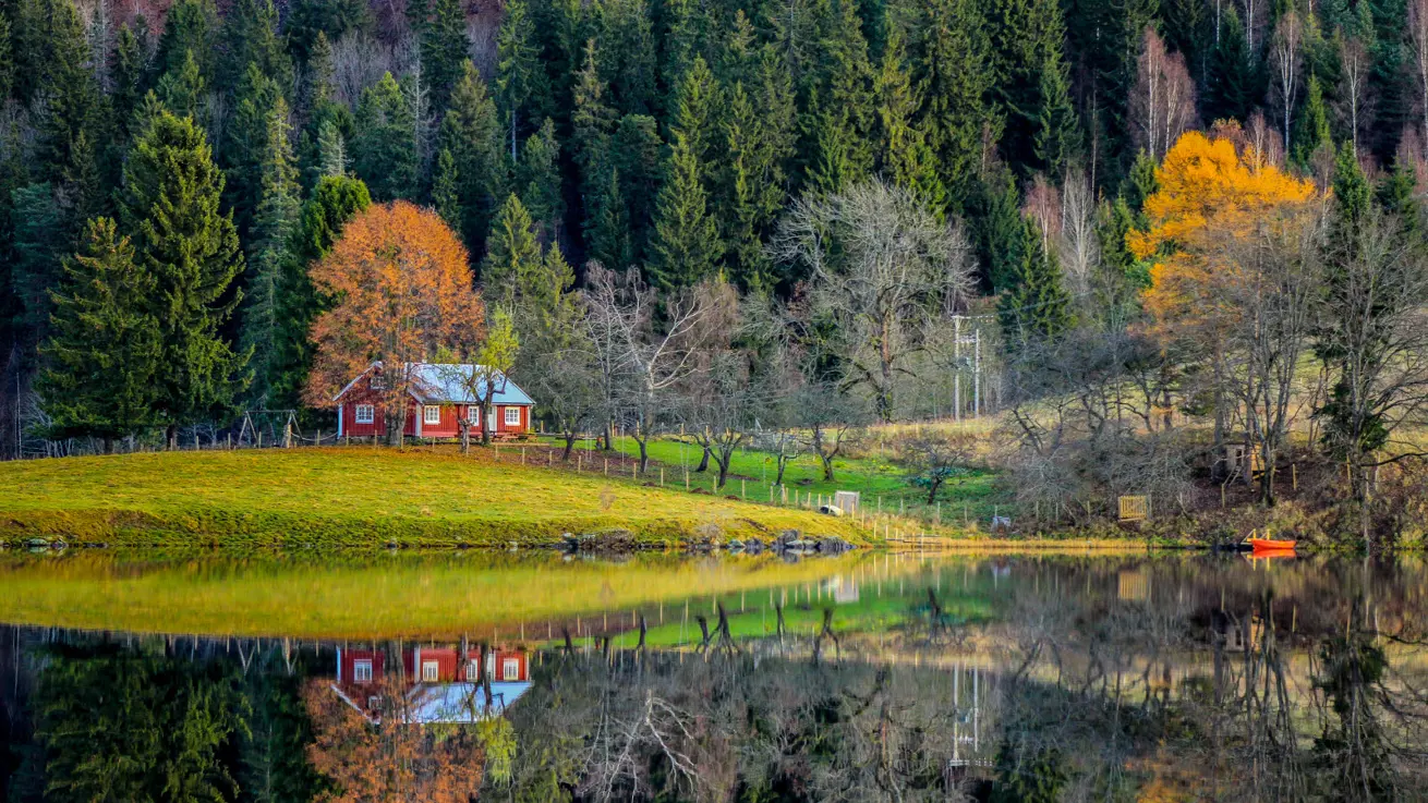 Semsvann i Asker. En rød hytte, med huskestativ utenfor. I forgrunnen ses vann. i bakgrunn skog i høstfarger.