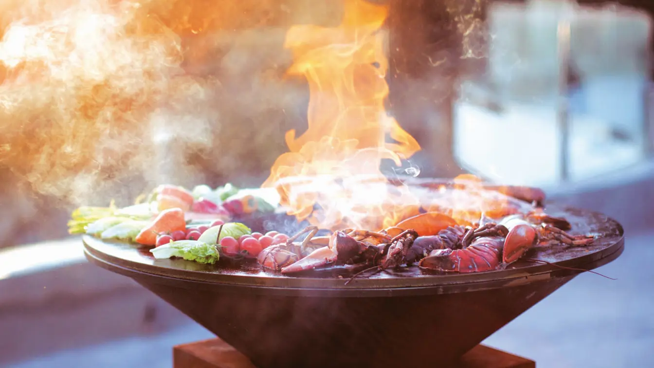 Round outdoor grill with flames, vegetables and seafood at restaurant Ask at Thon Hotel Vettre in Asker.