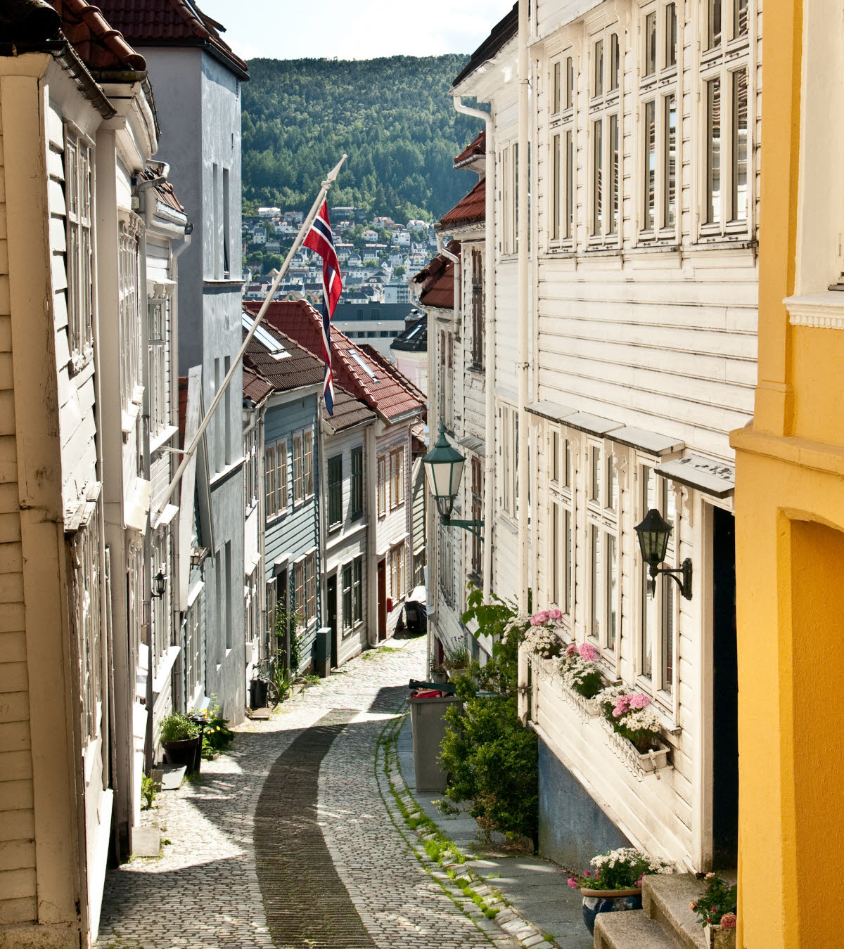 Karakteristieke steile straat in de oude stad van Bergen met Noorse vlag en schitterende zon.