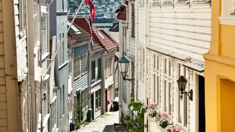 Karakteristieke steile straat in de oude stad van Bergen met Noorse vlag en schitterende zon.