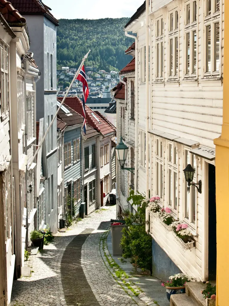 Characteristic steep alley in the historic neighbourhood of Bergen with Norwegian flag and shining sun.