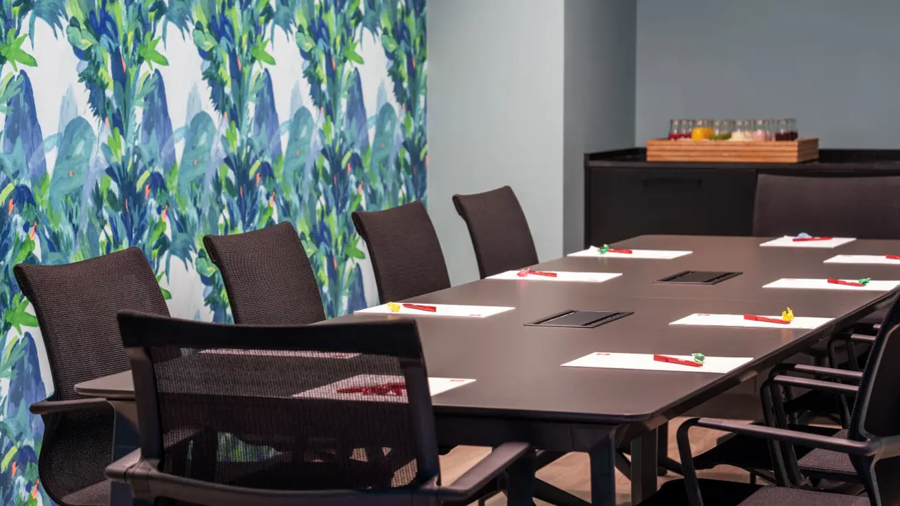 Meeting room in boardroom layout with office chairs, dark desk and patterned wallpaper.