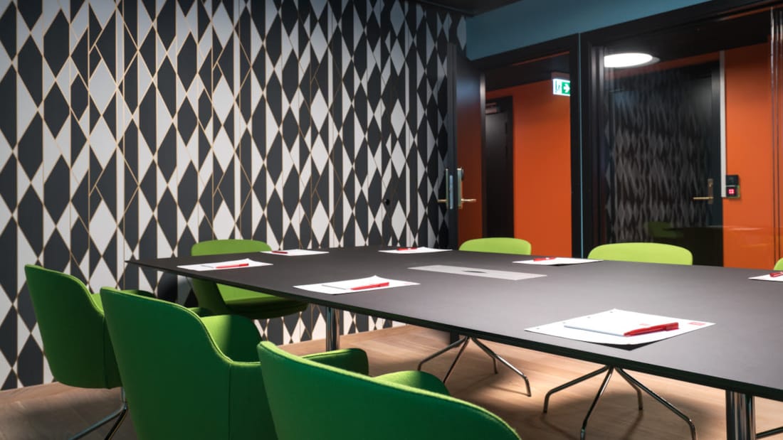 Grønne stole rundt om bestyrelsesbord med pen og papir og farverige vægge med mønster