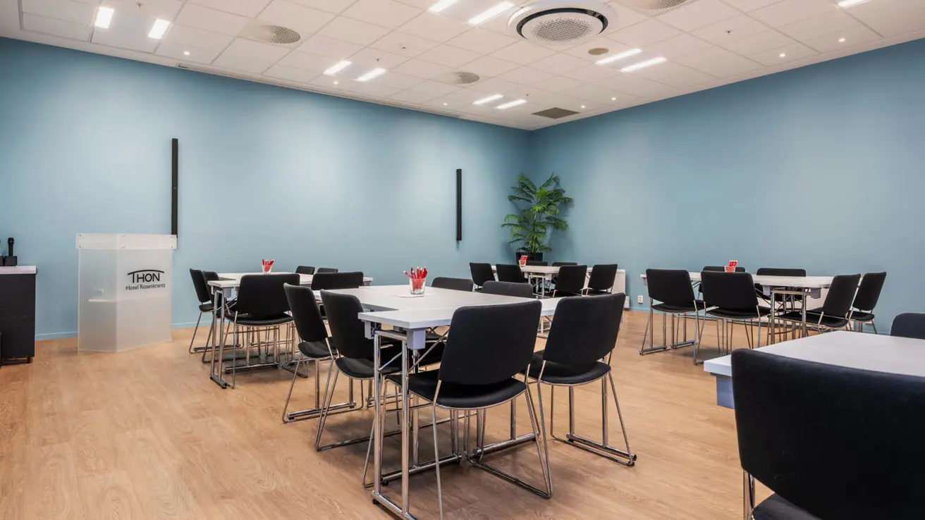 Møterom i gruppeoppsett. Talerstol i front.