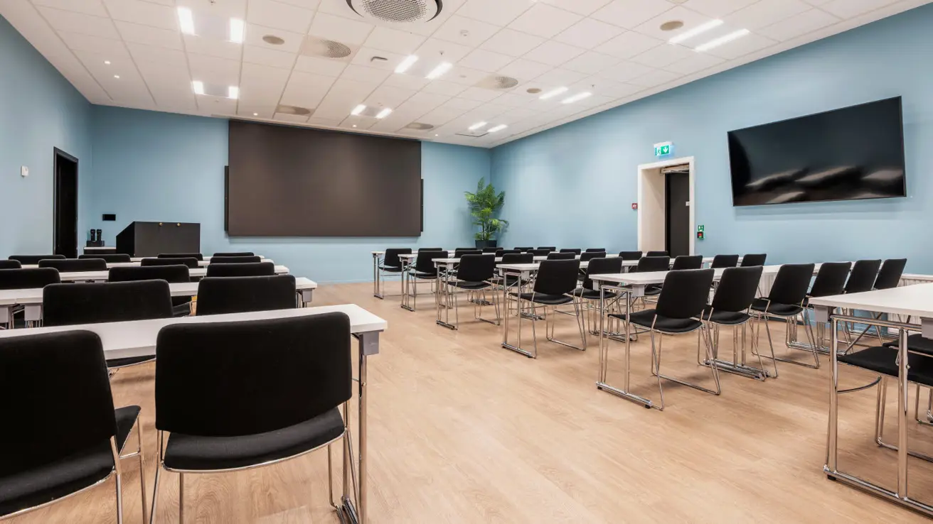 Konferanserom i klasseromsoppsett, skjerm i fornt og på siden.