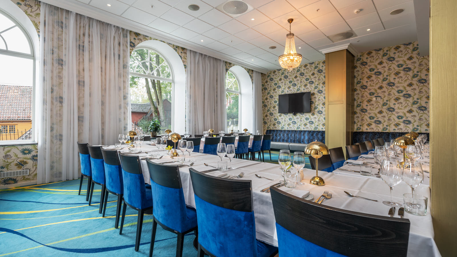 Lounge dekket til selskapsmiddag. Mønstrete tapet, teppebelagt gulv. utsikt mot baksiden av Bryggen.