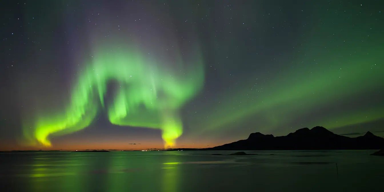Tanzendes grünes Nordlicht am Himmel mit etwas Orange am unteren Horizont.