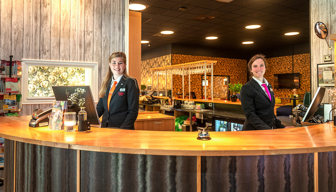 To kvinner som smiler bak resepsjonsdisken på Thon Hotel Bjørneparken