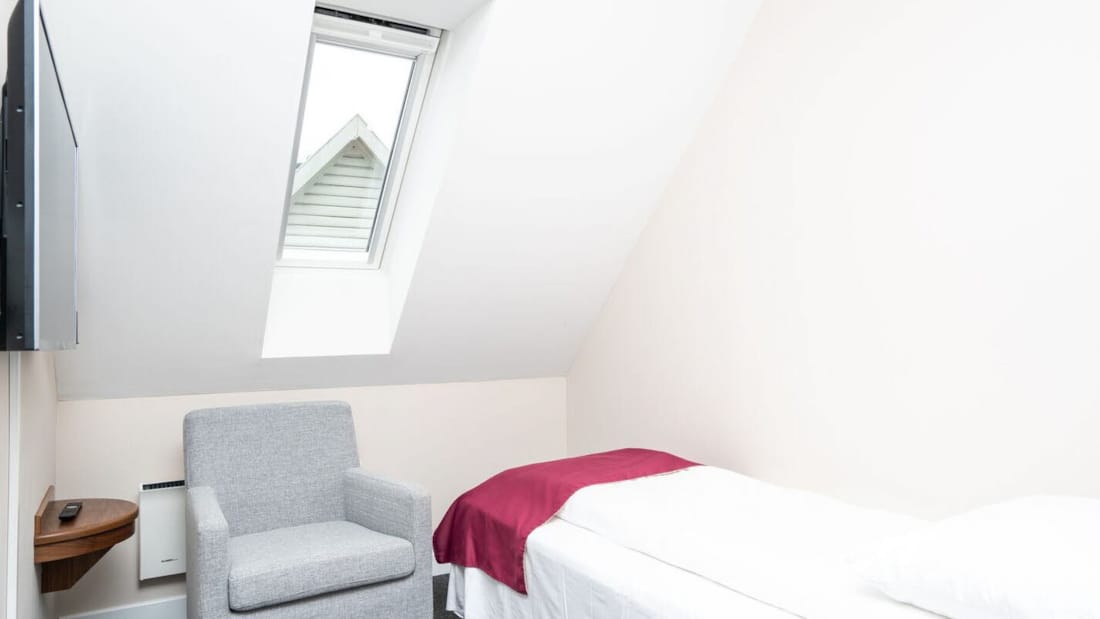 Säng, fåtölj och tv i enkelrum på Hotel Førde