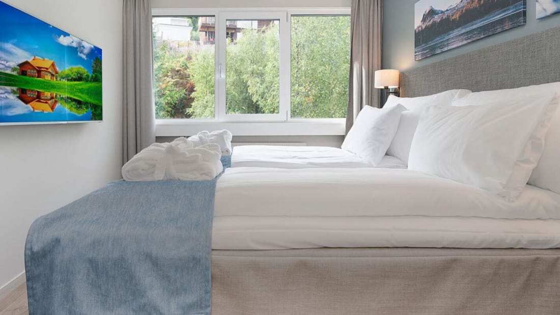 Store senge med tv-skærm og lyst vindue med udsigt mod grønne omgivelser