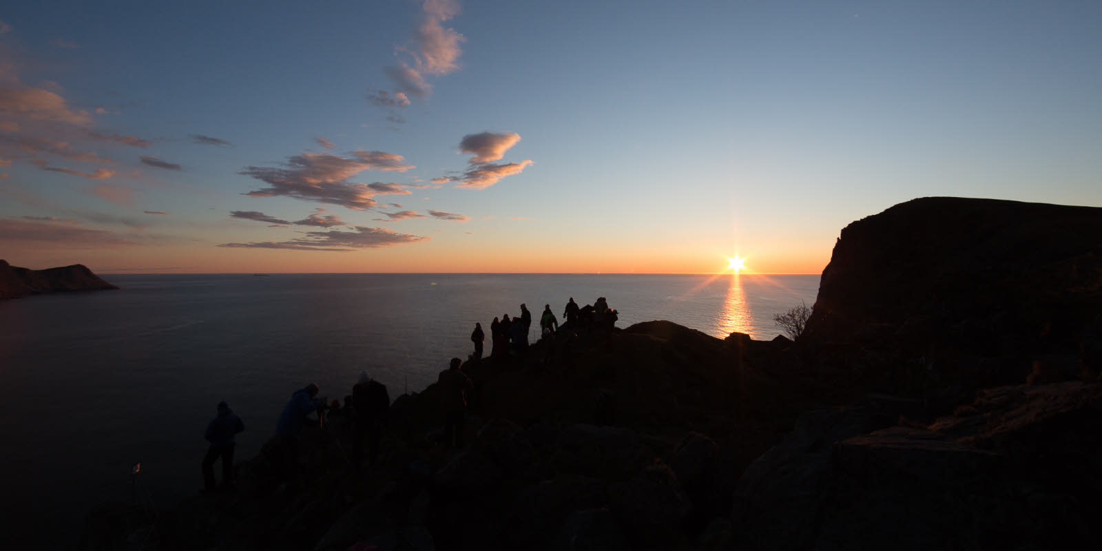People standing on a cliff overlooking the sea at sunset.