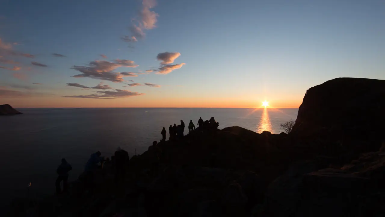 Des gens se tiennent sur une falaise et regardent la mer au coucher du soleil.