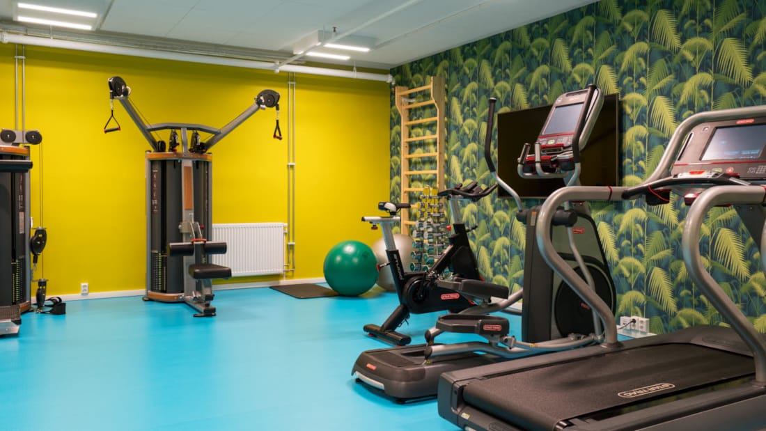 Fitness-rum med gule vægge og turkis gulv med forskellige træningsmaskiner på Thon Hotel Gardermoen