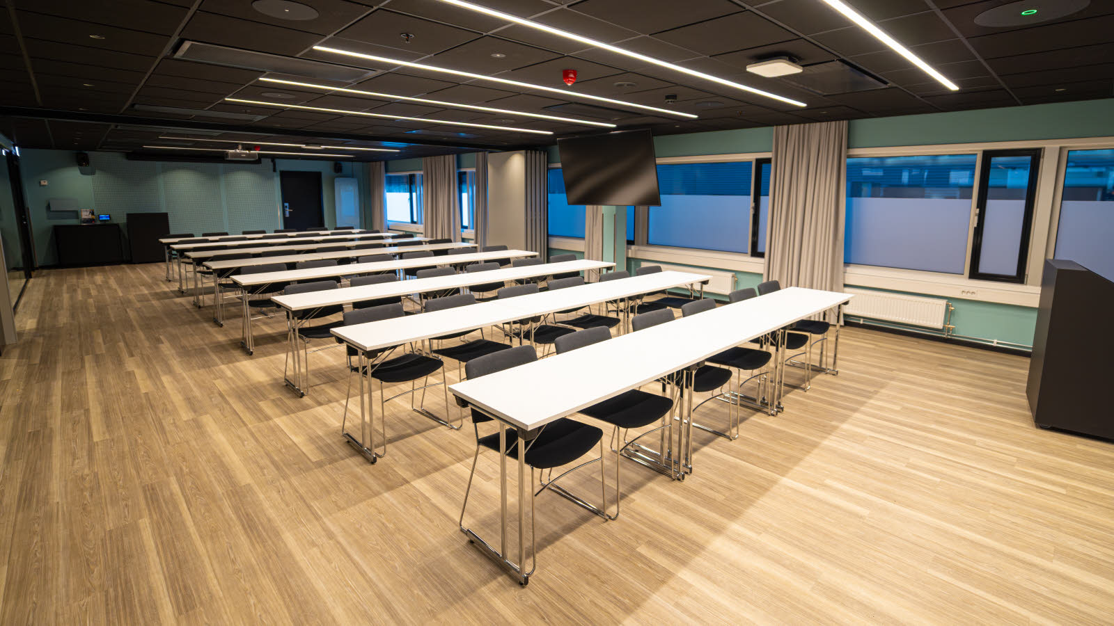 Stort og luftig møterom med bord og stoler i klasseromsoppsett.