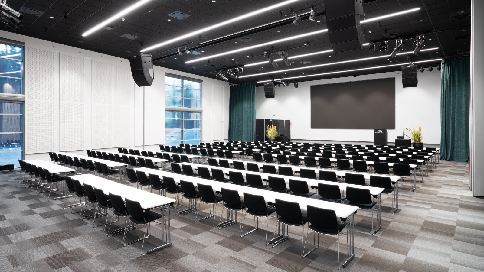 Stort og luftig konferanserom med bord og stoler i klasseromsoppsett. 