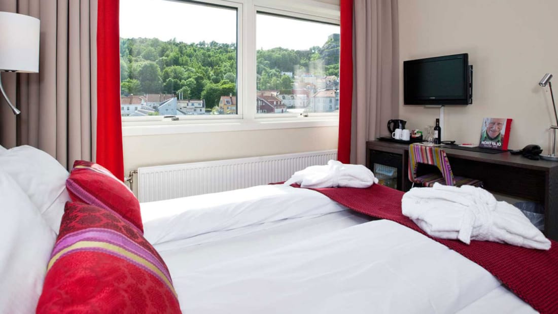 Superior værelse med redt seng og røde puder i lyst værelse med TV