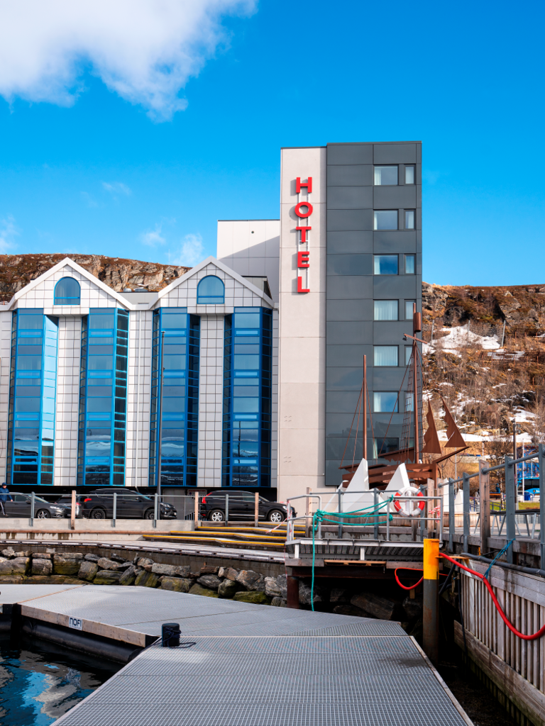 De gevel van Thon Hotel Hammerfest gezien vanaf het kustgebied. Blauwe hemel op de achtergrond.