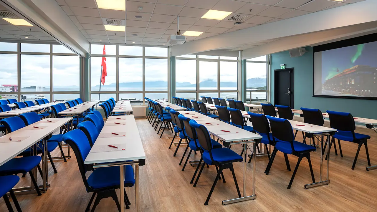 Grande et lumineuse salle de réunion du Thon Hotel Harstad. Table et chaises bleues en classe. Grandes fenêtres en arrière-plan.
