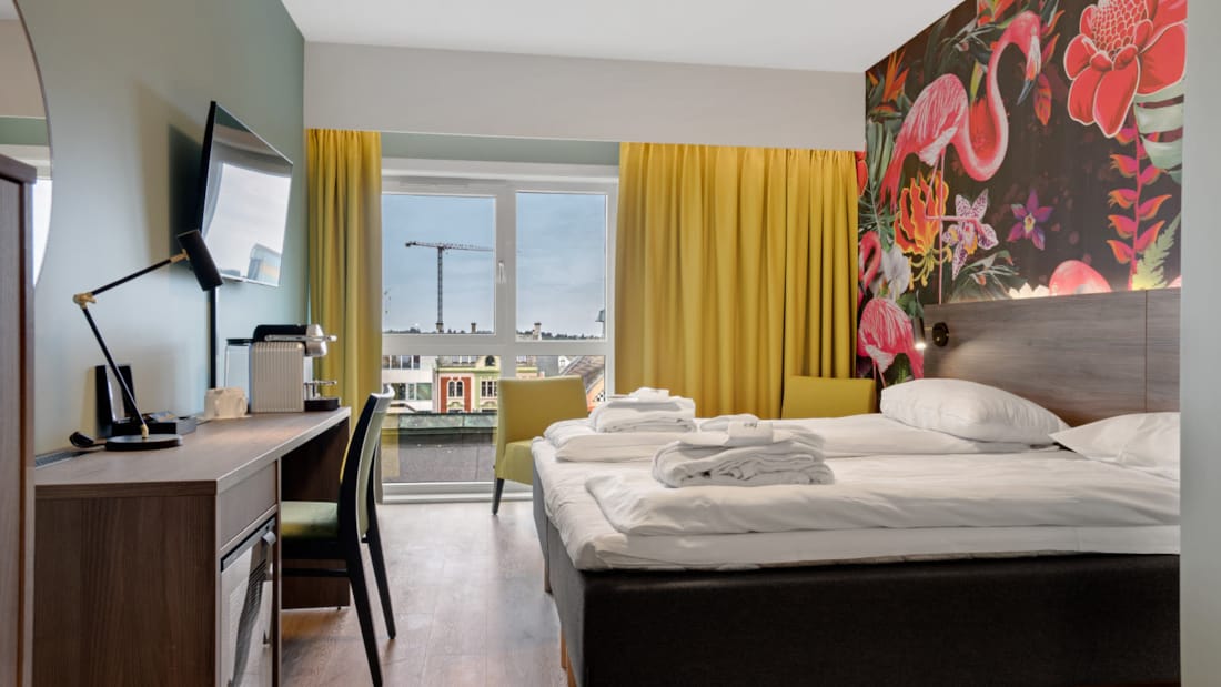Dobbeltseng Thon Partner Hotel Saga farverigt tapet med flamingoer og lyst værelse med stort vindue og skrivebord