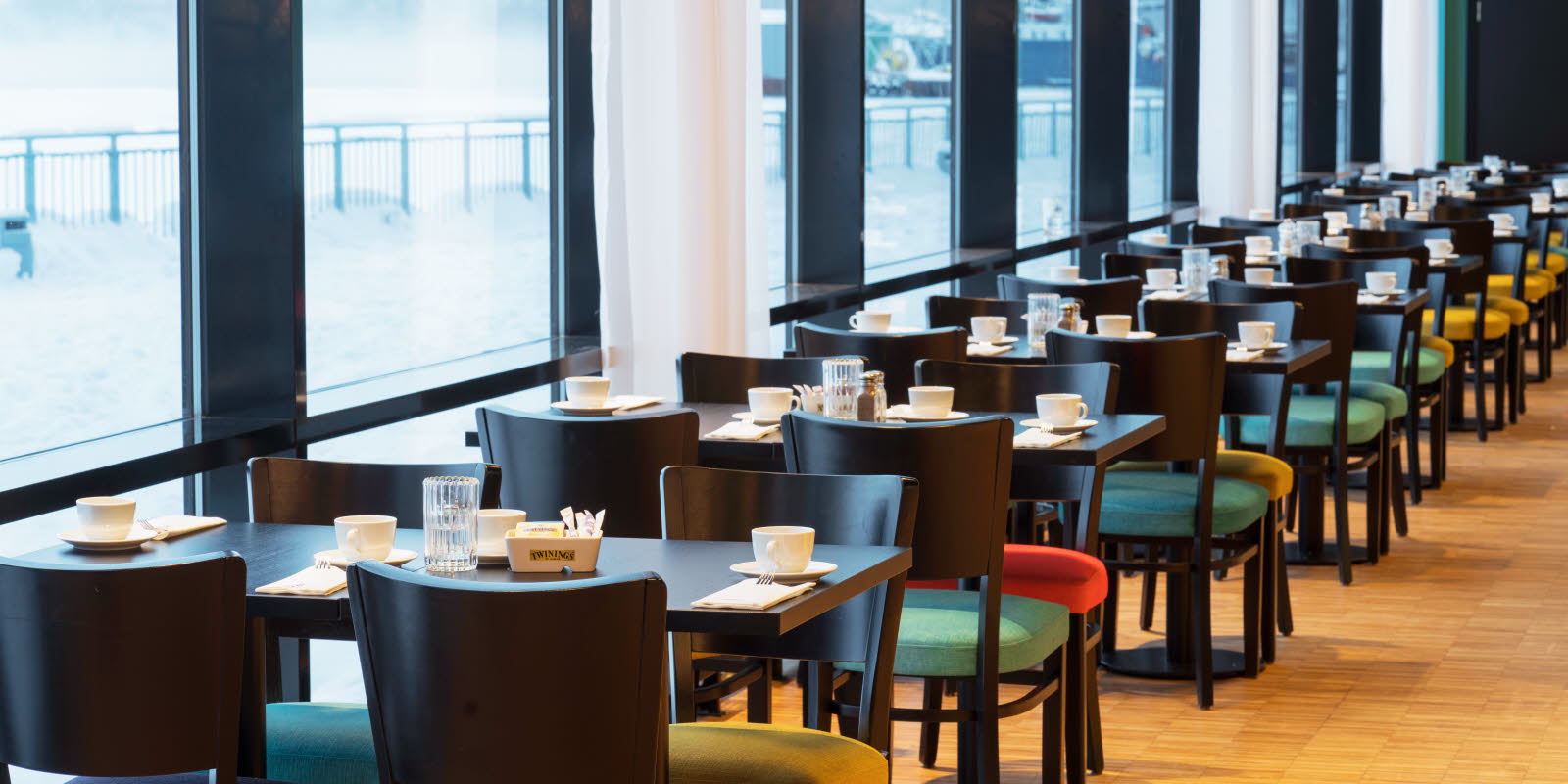 Borde i morgenmadssal med store vinduer  med udsigt mod kajen og havet på Thon Hotel Kirkenes ved kajen i Kirkenes centrum