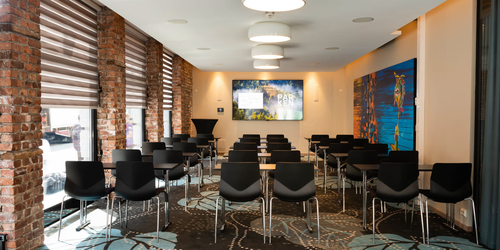 Eik konferencelokale med klasseværelsesopsætning set mod skærm