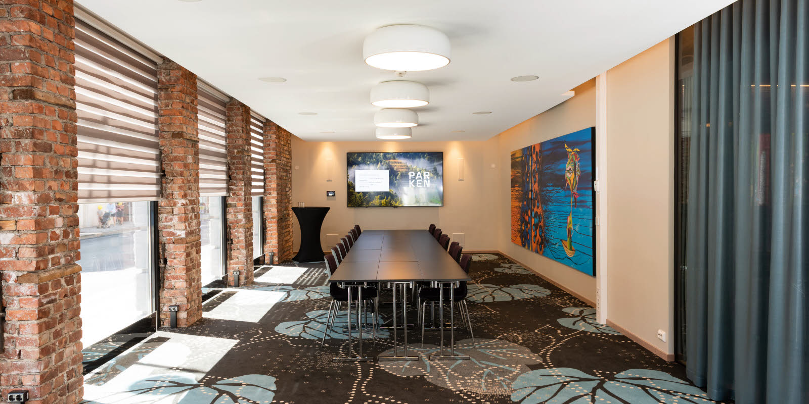 Eik konferencelokale med bestyrelsesbord set mod skærm