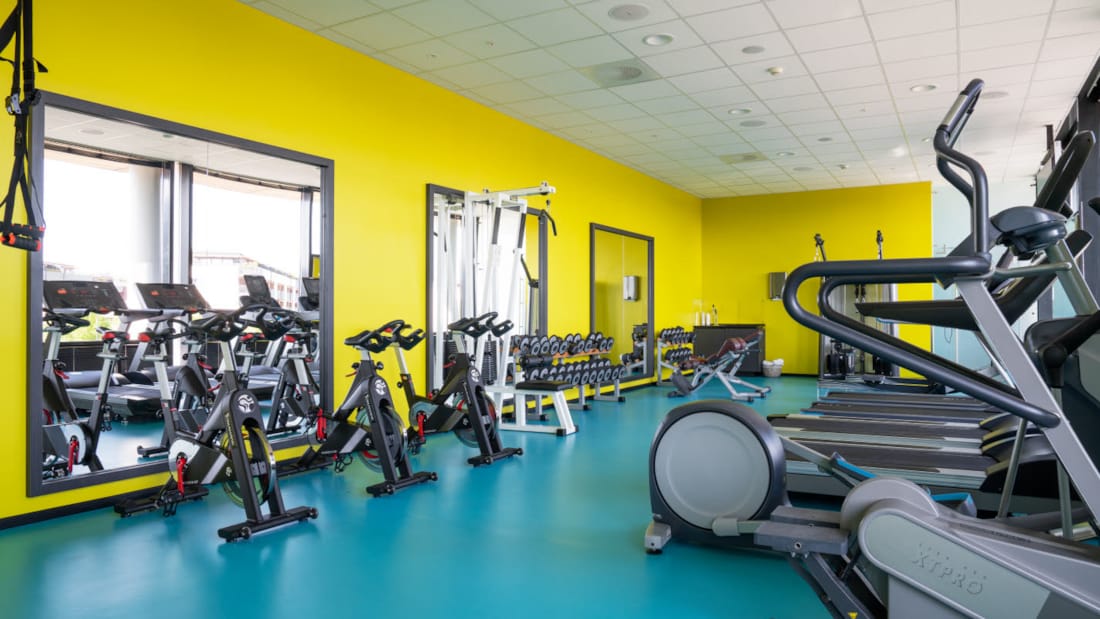 Diverse træningsmaskiner med gule vægge og turkis gulv i træningslokalet på Thon Hotel Arena i Lillestrøm