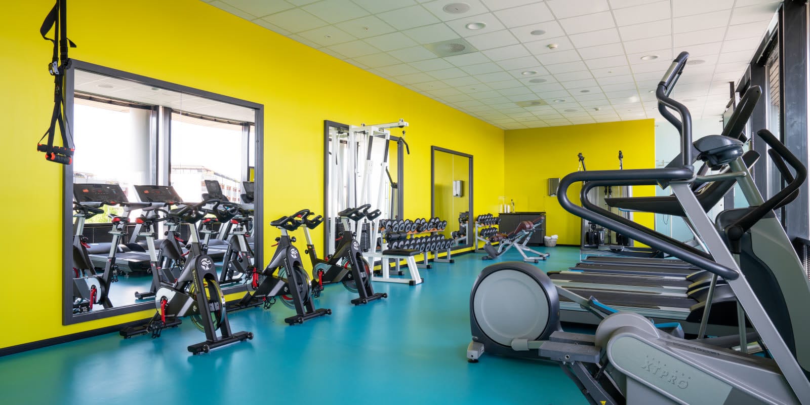 Gula väggar och turkosa golv i gym med diverse träningsredskap på Thon Hotel Arena i Lillestrøm
