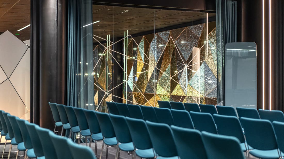 Illustration de la salle de conférence Jostedalsbreen en configuration de banquet. Beaucoup de grandes surfaces vitrées, grand écran sur le mur du fond.