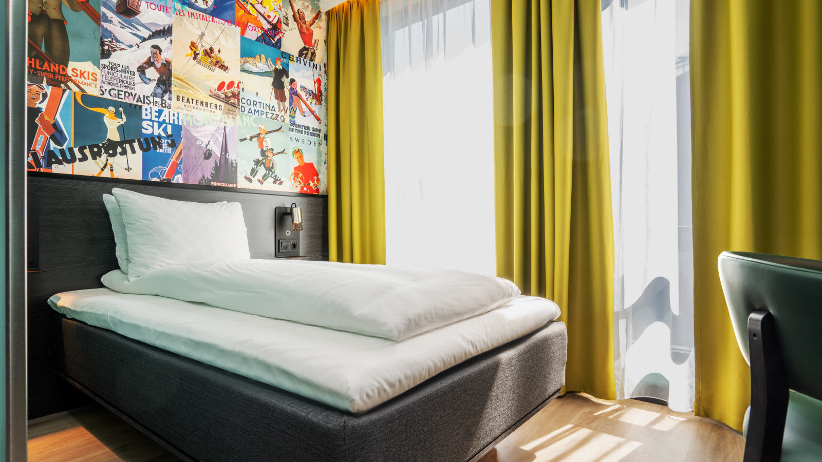 Neatly made double bed in front of two large windows with yellow curtains