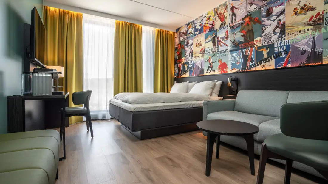 Superior room with double bed, desk, chair, sofa, coffee table, floor-to-ceiling windows, wallpaper with ski motifs.