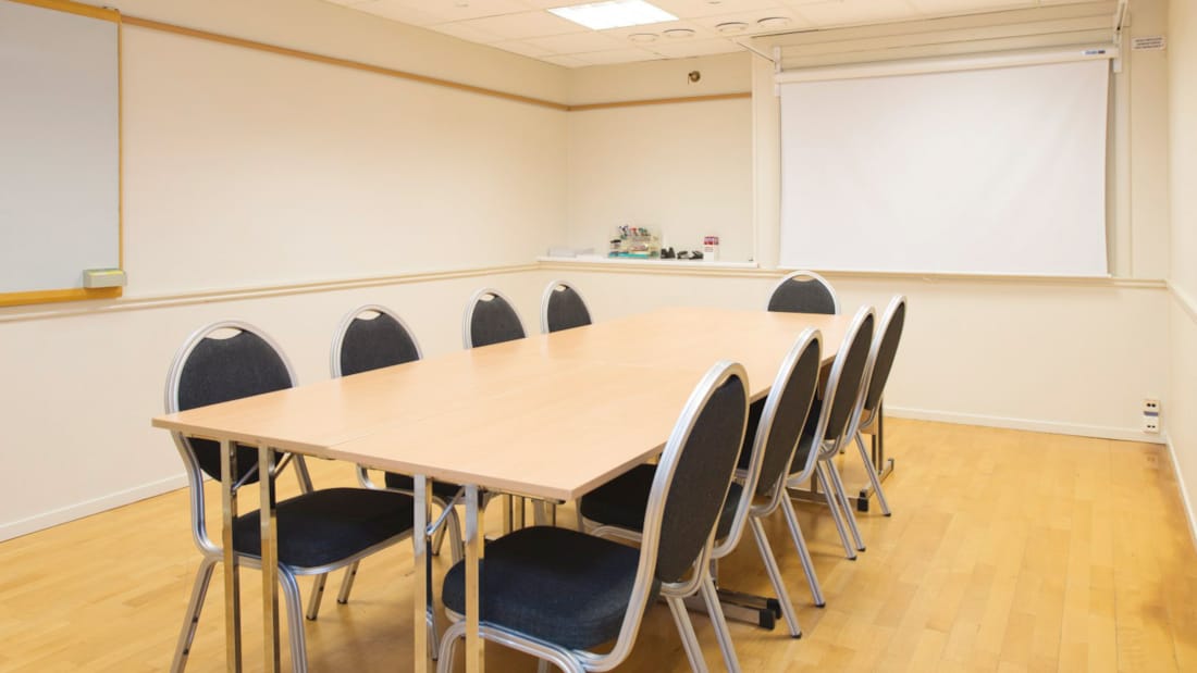 Salle de réunion avec table longue, chaises noires, tableau blanc et projecteur