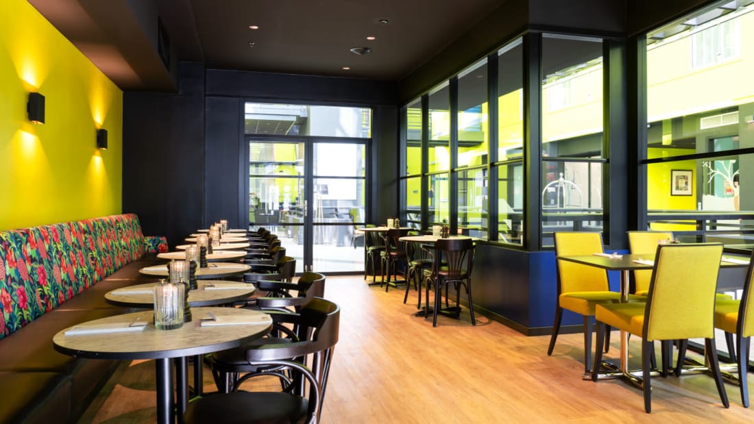 Restaurant med siddepladser med gul væg, gule stole og sorte møbler mod lobby i business room på Thon Hotel Triaden i Lørenskog