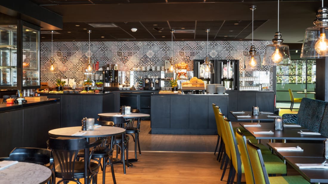 Restaurant med siddepladser, set mod køkken og buffetområdet med mønstrede fliser på væggen på Thon Hotel Triaden i Lørenskog